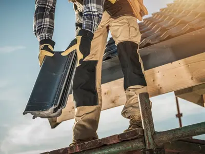 Ouvrier portant une tuile sur une toiture en chantier